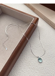 Detail of S925 sterling silver necklace with light blue oval gemstone on wooden tray