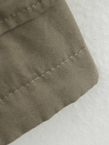 Detail of khaki canvas jacket showing reinforced double stitching and plain weave texture