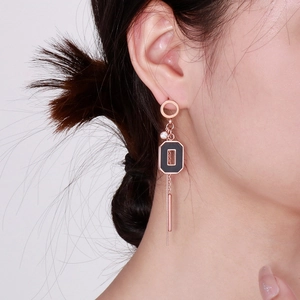 Détail de boucles d'oreilles rose doré avec émail noir et pompons à chaînettes