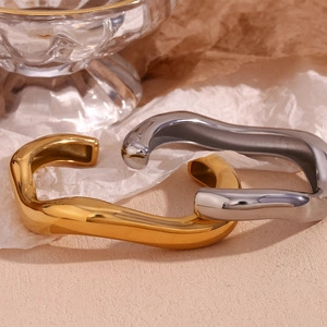 Minimalist liquid wave 18K gold and silver open bangles set on a textured background
