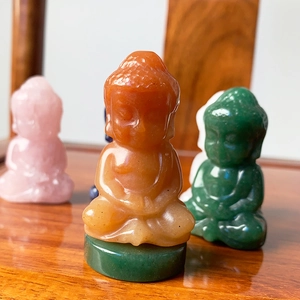 Macro shot of orange natural crystal Buddha statue on green base with blurred background