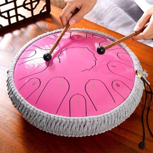 Pink steel tongue drum with woven base and wooden mallets on a traditional wood desk