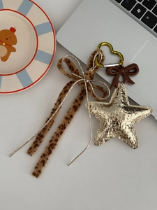 Detail of star charm and leopard print ribbon keychain on a white tabletop