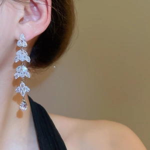 Close-up of sparkling silver leaf tassel earrings worn by a model in warm lighting