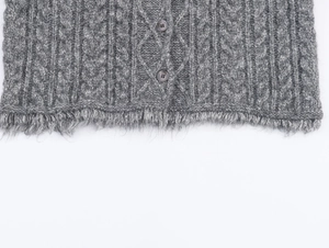 Dettaglio del cardigan grigio a trecce con texture morbida e orlo con nappe decorative