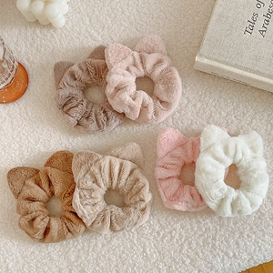 Detail of plush cat-ear scrunchies in multiple soft colors on a cozy warm white background