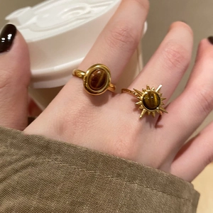 Close-up of golden oval tiger eye stone ring worn by model holding white coffee cup