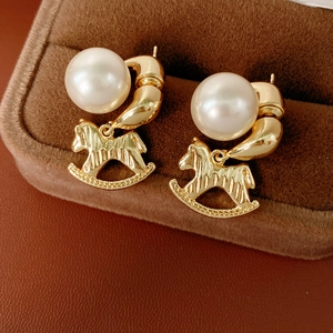 Détail de la boucle d'oreille cheval à bascule dorée avec perle en boîte à bijoux