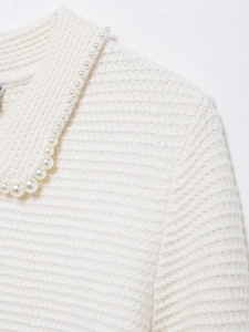 Détail d'un pull en tricot blanc avec texture à grosses mailles et chaîne de perles