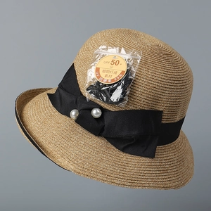 Detail of straw sun hat featuring a wide black ribbon bow and elegant pearl accents