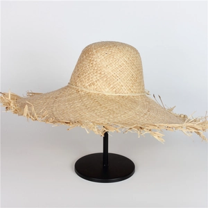 Detailed close-up of natural raffia straw hat showing wide brim fringe and woven texture