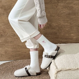 Close-up of fuzzy white thermal socks with pink bow embroidery and brown buckle mules