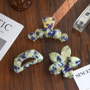 Three marble texture floral hair clips in blue, purple, and yellow on a wooden desk