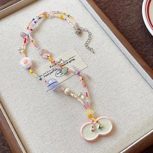 Close-up of a colorful beaded necklace with ceramic flower and bow charms on a linen tray