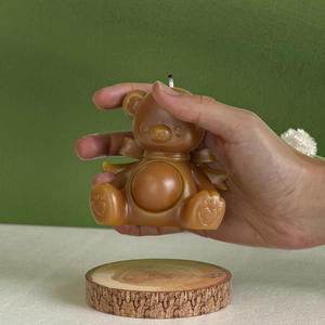 Brown bear candle with a bow tie and heart detail shown on a natural wood base