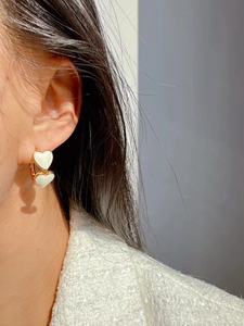 Close-up of model wearing gold double heart earrings with white enamel finish
