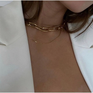 Close-up of a chunky gold link chain layered with a sleek snake necklace on a model