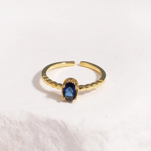 Detailed shot of an adjustable gold ring with blue oval stone on white textured rock