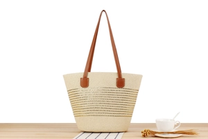 Close-up of beige woven straw tote with gold stripes and brown leather shoulder straps