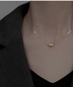 Close-up of a gold bean pendant necklace on a model wearing a black suit jacket