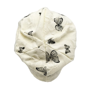 Close-up of beige knit beanie with distressed butterfly prints and textured ripped fabric
