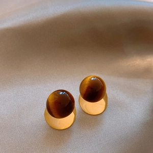 Macro view of gold stud earrings with tiger eye stone spheres on champagne silk fabric