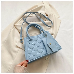 Detail view of light blue quilted crossbody bag with matching mini pouch on a beige blazer