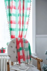 Detail of red and green plaid Christmas curtains with white fringe in a cozy home setting