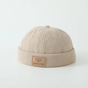Close-up of beige corduroy beanie featuring a cute bear leather patch and ribbed texture