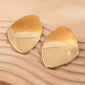 Dettaglio macro di orecchini dorati irregolari su un vassoio in legno minimalista