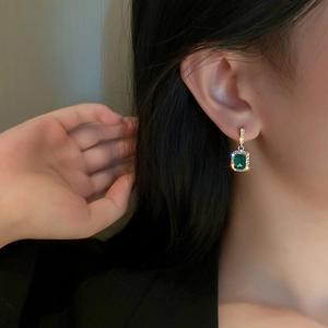 Close-up of elegant emerald green rectangle earring with sparkling cubic zirconia halo