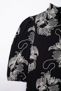 Close-up of white floral embroidery on a black cotton linen shirt with puff sleeves