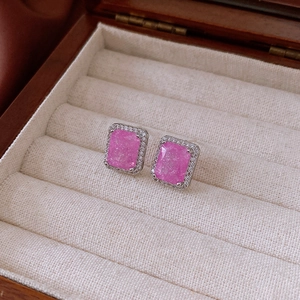 Close-up of pink square zircon earrings in a wooden jewelry box with a halo setting