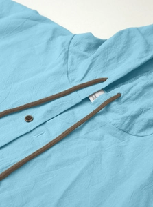 Detailed close-up of sky blue linen blend shirt fabric texture with drawstrings and buttons