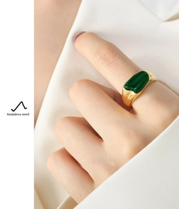 Macro detail of irregular gold stainless steel ring with green rectangle stone on finger