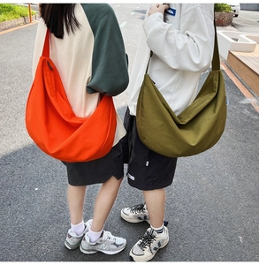 Outdoor shot of oversized half-moon nylon crossbody bags in bright orange and olive green