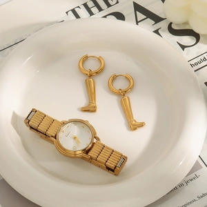 Schicke goldene Ohrringe in Stiefelform und Metalluhr auf einem Keramiktablett