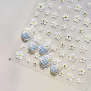 Detail of 3D white flower nail stickers and blue plaid design on manicure tips