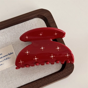 Macro detail of a red acetate hair claw clip featuring sparkling rhinestones and golden dots