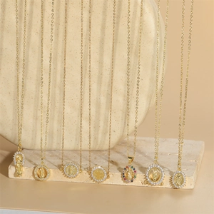 Minimalist gold Virgin Mary pendants with zircon stones on stone background