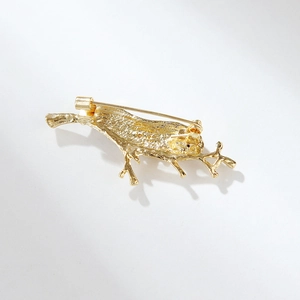 Golden bird on branch brooch with detailed metal texture and secure back pin