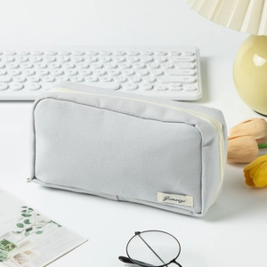 Close-up of light grey canvas pencil case with zipper and label on a desk setup