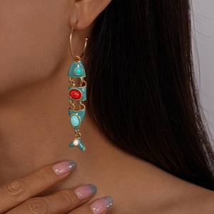 Detailed close-up of a gold fish-shaped earring with turquoise and red enamel on model