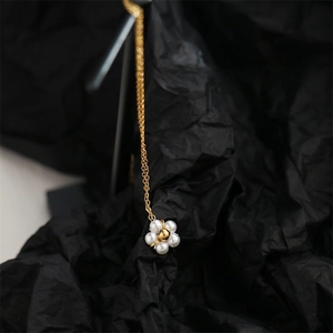 Detailed shot of golden flower pendant with white pearls on a thin chain necklace