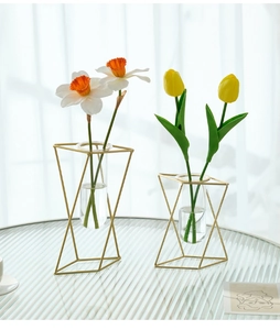 Detail of geometric gold metal frame with glass test tube vase on textured glass