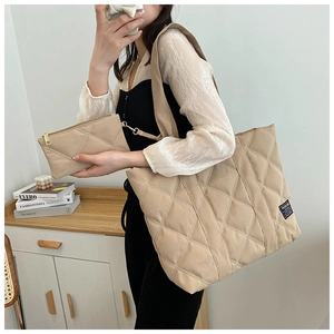 Detail of beige quilted tote bag set with matching pouch worn on shoulder by model