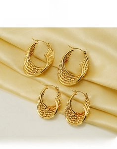 Macro shot of gold-plated titanium steel layered twisted hoop earrings on satin