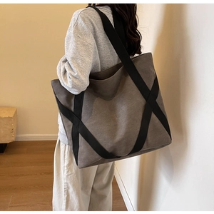 Detail view of large canvas tote bag with black webbing straps on model's shoulder