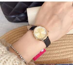 Detail of elegant gold watch with diamond bezel and black leather strap on female wrist