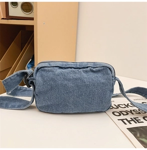 Detail shot of the washed blue denim texture and top zipper on a crossbody bag